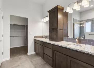 Two vanities with granite countertops and built in drawers, and an above counter cabinet separate his and hers bathroom space.